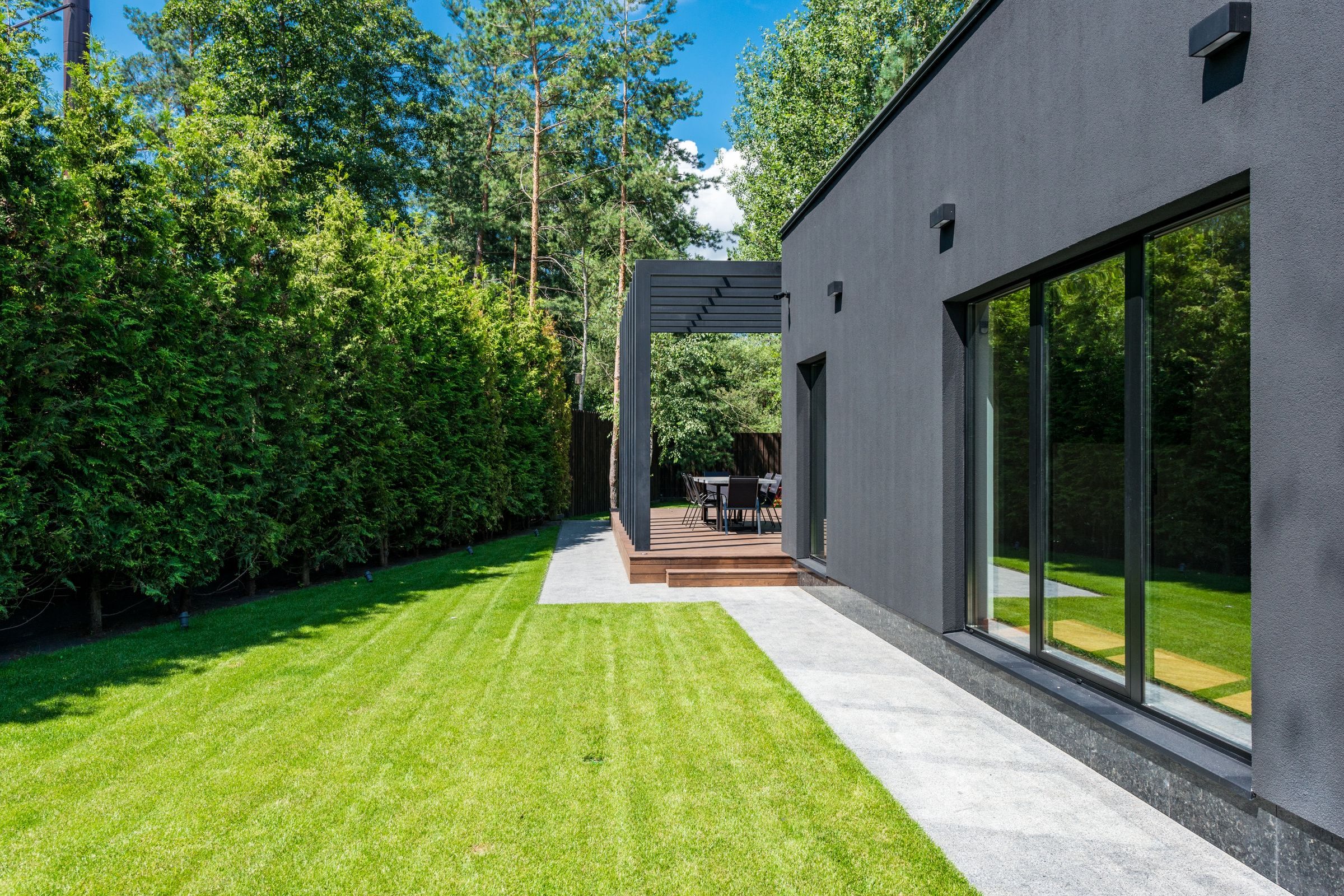 Frisch gemähter Rasen mit hoher Hecke neben einem modernen Haus